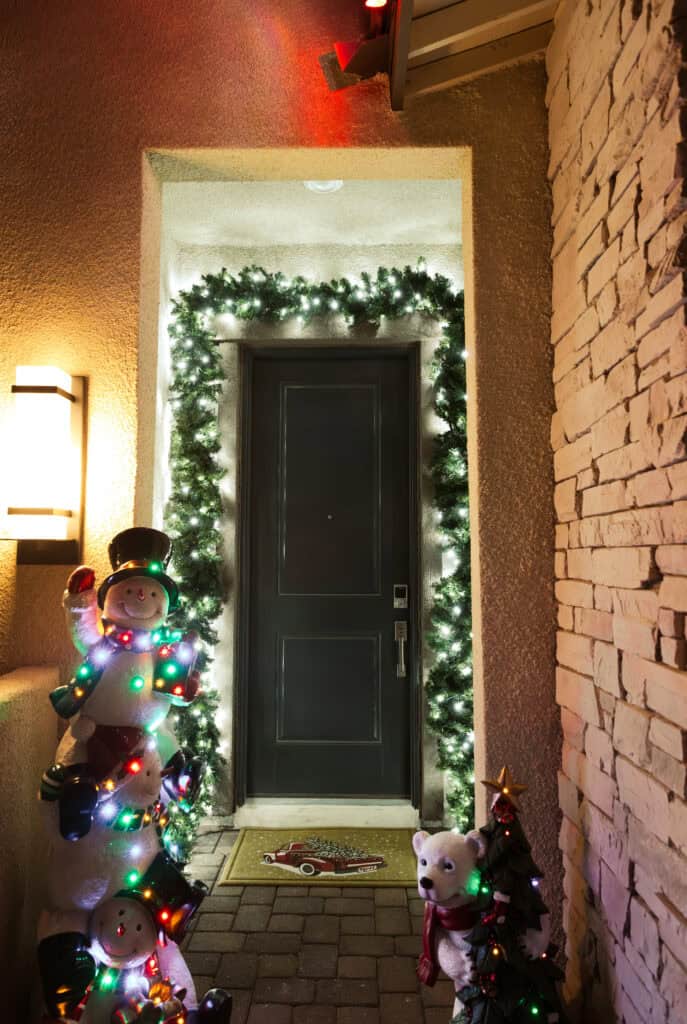 Front door of stucco home decorated with Pure white christmas garland and snowmen, polar bear, Christmas tree decorations