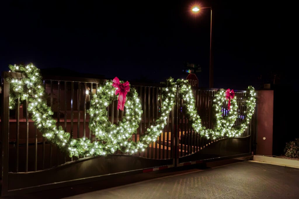 Warm white lighted garland with red bows on an HOA entrance gate