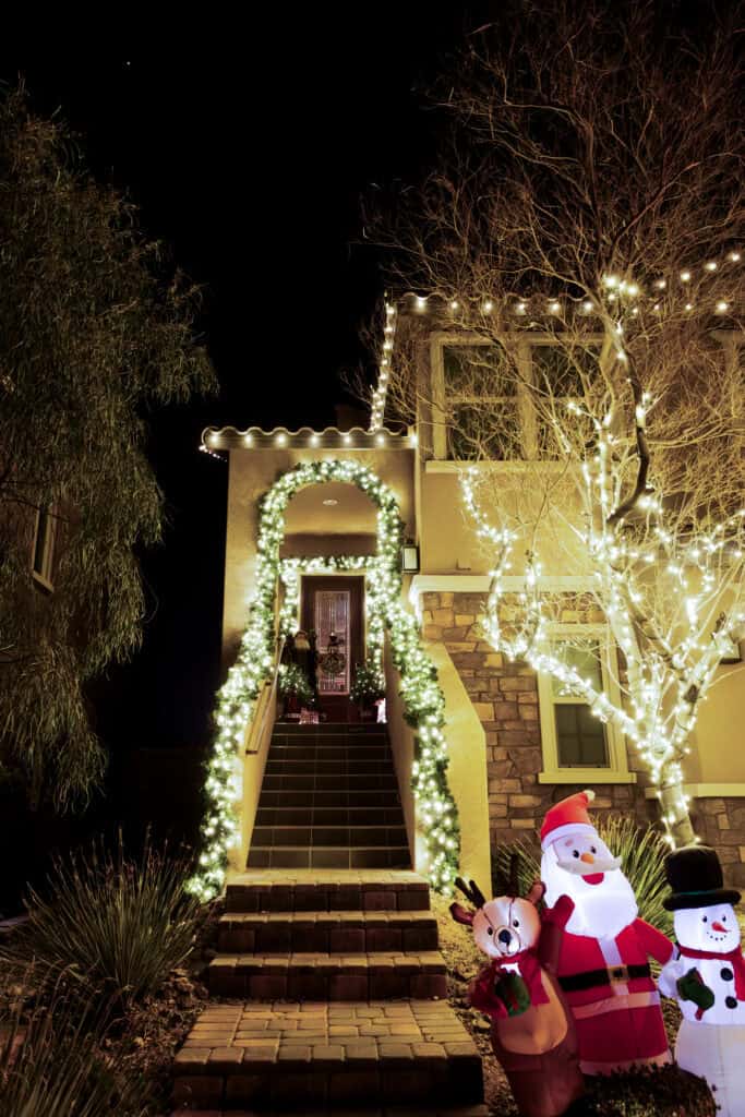 Warm White Christmas lights installed along roof and front stairs with lit warm white garland along railing and front door