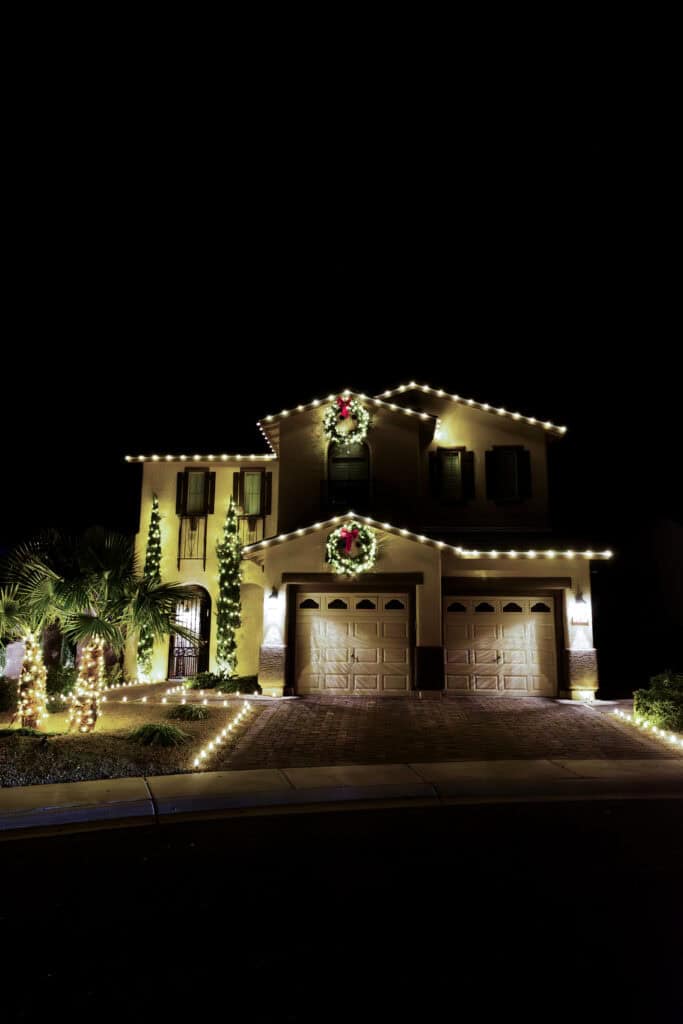 Warm white lights installed with matching lit christmas wreaths installed above garage and top of house. Warm white christmas lights installed on palm trees and along driveway
