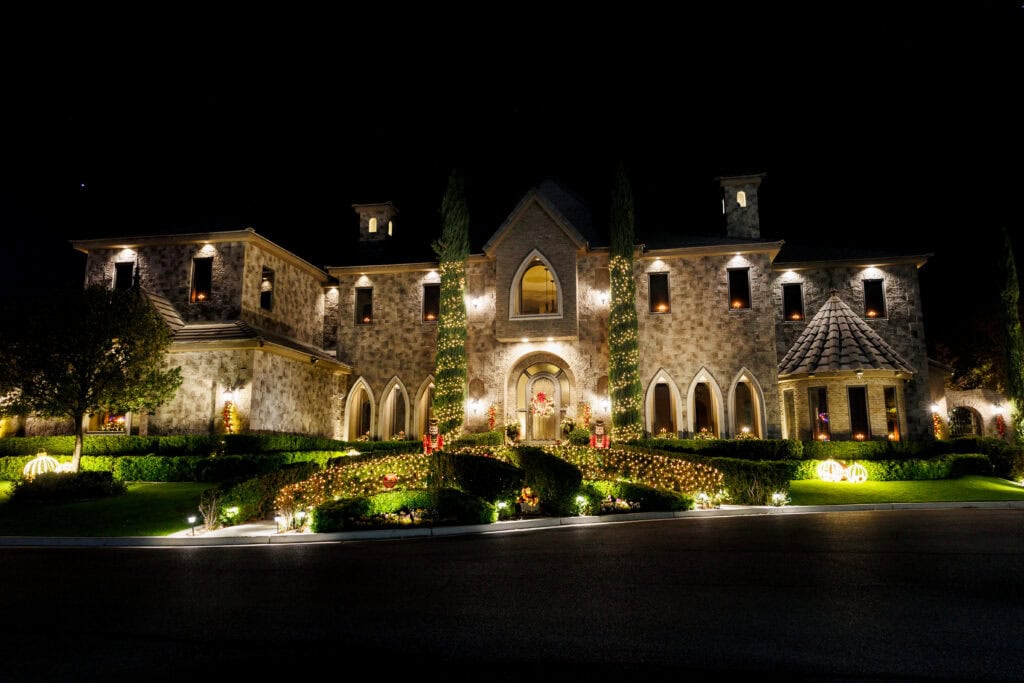 Christmas lights installed on a large home around the trees and bushes, outlining the walkway and around the door by Top Christmas light installers in Houston, Texas - Lights Up USA is the top installer of christmas lights for homes and businesses in Austin, Houston, Phoenix, and Las Vegas