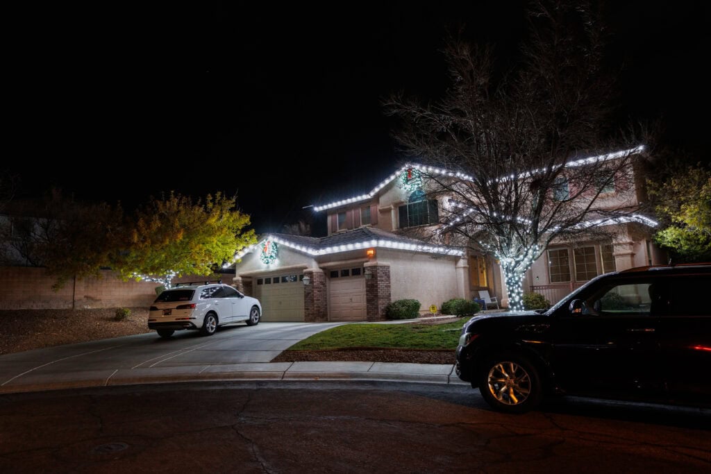 Pure white Christmas lights on a roofline with a lit tree